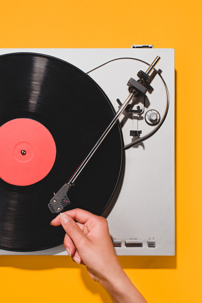 cropped shot of woman turning on vinyl player isolated on yellow - Foto, Bild