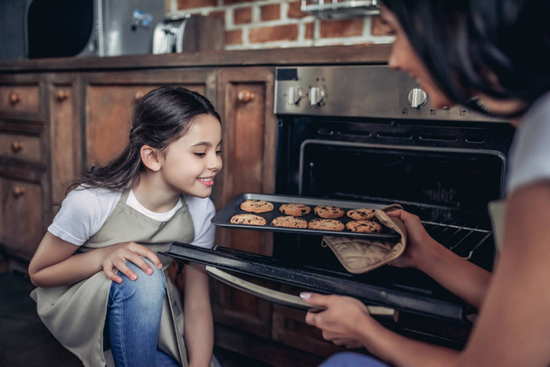 portrait of girl smelling fresh backed cookies with her mother on the kitchen - Fotó, kép