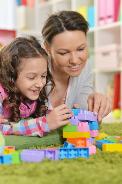 Pequeña niña rizada y su madre jugando con bloques de plástico de colores en casa
 - Foto, Imagen