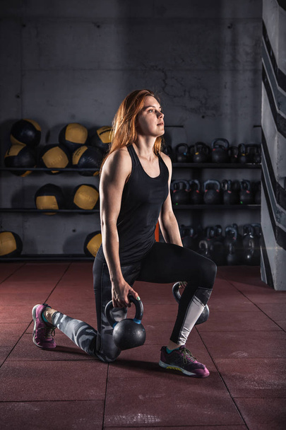 Ελκυστική νεαρή γυναίκα κάνει ασκήσεις με kettlebell. Άρση βαρών και τη δύναμη ανύψωσης workout. Σπορ, γυμναστήριο έννοια. - Φωτογραφία, εικόνα