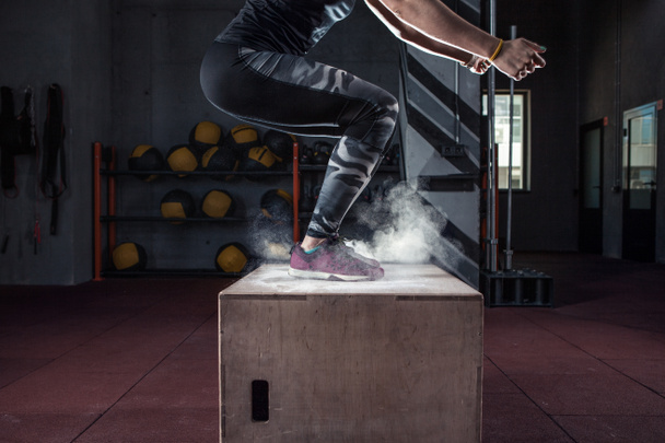 mujer joven salto caja y talco polvo sale de debajo de los pies. Mujer de fitness haciendo entrenamiento de salto de caja en el gimnasio de cross fit
. - Foto, Imagen