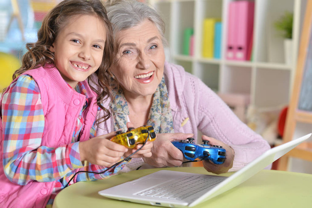 Portret van verrast grootmoeder en dochter spelen van computerspel met laptop  - Foto, afbeelding