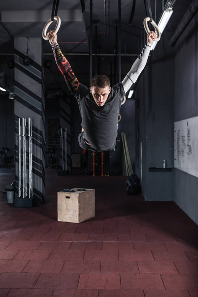 Muscle-up exercise athletic man doing intense workout at the crossfit gym on gymnastic rings - Φωτογραφία, εικόνα