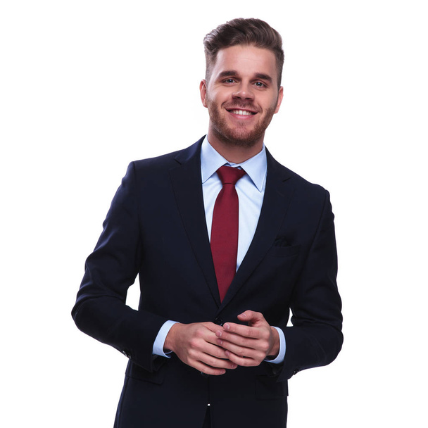 portrait of happy young businessman fixing his navy suit sleeves while standing on white background - Foto, imagen