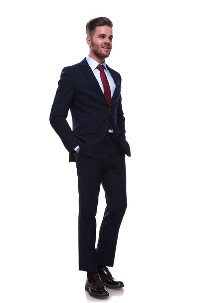 sexy hombre de negocios relajado en traje azul marino y corbata roja se ve a un lado mientras está de pie sobre fondo blanco
 - Foto, Imagen