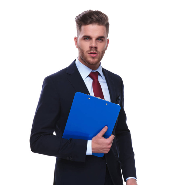 Porträt eines gutaussehenden Geschäftsmannes mit blauem Klemmbrett auf weißem Hintergrund, der verführerisch und ernst wirkt - Foto, Bild