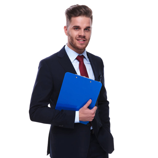 portrait d'homme d'affaires souriant avec un dossier à la main debout sur fond blanc. Il porte un costume de marine et une cravate rouge.
 - Photo, image