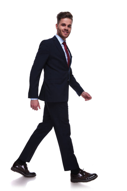 Geschäftsmann in Marine-Anzug und roter Krawatte tritt zur Seite auf weißem Hintergrund, Ganzkörperbild - Foto, Bild