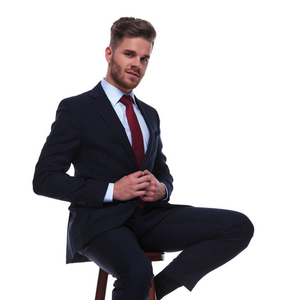 ελκυστική νεαρή επιχειρηματίας κουμπώματος του Ναυτικού κοστούμι σε λευκό φόντο. Κάθεται σε μια ξύλινη καρέκλα, φωτογραφία πορτραίτου - Φωτογραφία, εικόνα
