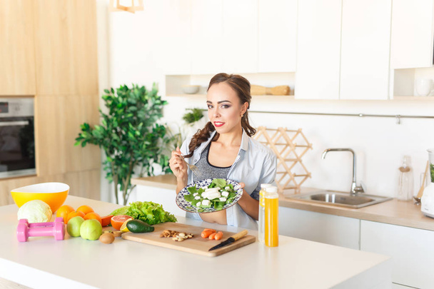 Petite and fit brunette caucasian girl eating salad during cooking at kitchen  - Φωτογραφία, εικόνα