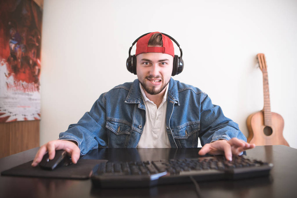 Joueur de casque concentré joue à des jeux à la maison sur un ordinateur. Homme dans une veste en denim assis à la table et joue à des jeux sur un ordinateur à la maison. Concept de jeu vidéo
. - Photo, image