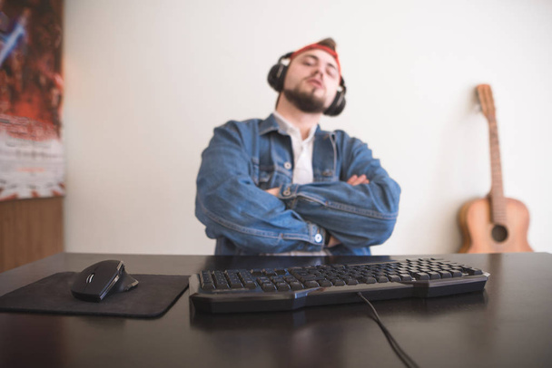 Portrait of a gamer with a beard and a denim jacket at a computer desk. Focus on the keyboard and mouse. - Fotografie, Obrázek