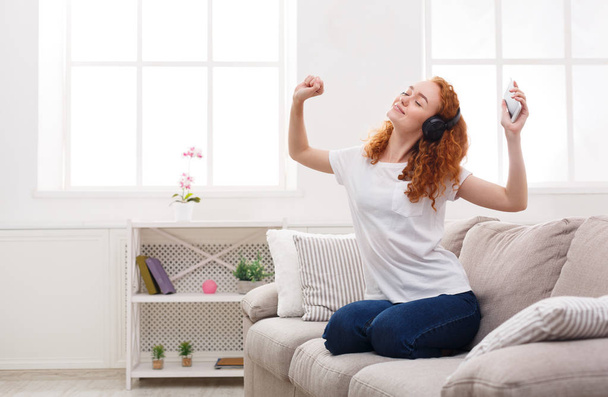 Happy redhead woman enjoying her favorite song in earphones - Photo, Image