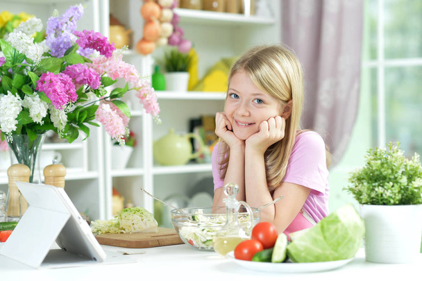 Το χαριτωμένο μικρό κορίτσι με φρέσκια σαλάτα σε γυάλινο μπολ στο τραπέζι της κουζίνας - Φωτογραφία, εικόνα