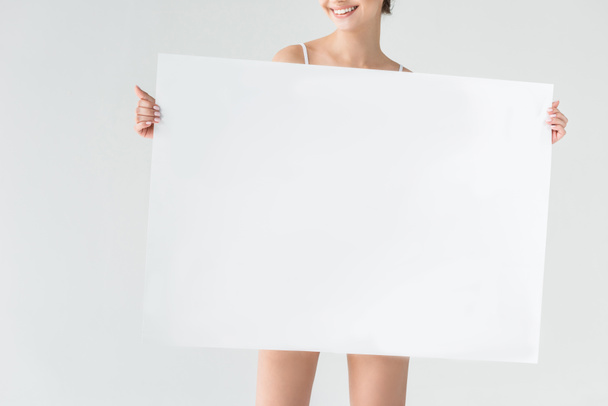 灰色の背景に分離された白紙の横断幕を持って笑顔の女性のトリミングされた画像  - 写真・画像