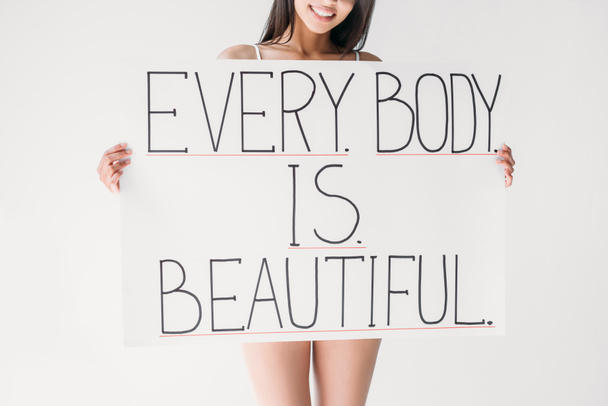 abgeschnittenes Bild einer lächelnden Frau mit Banner mit Schriftzug Jeder Körper ist schön isoliert auf grauem Hintergrund - Foto, Bild