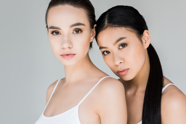portrait of attractive asian and caucasian young women looking at camera isolated on gray background  - Photo, image
