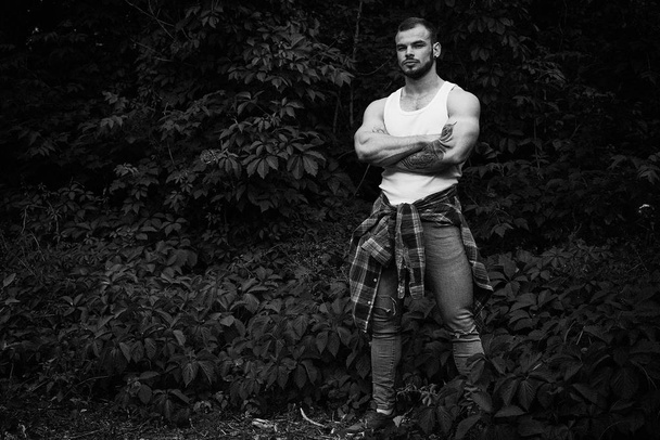 Black and white photo of handsome young masculine man posing outdoors in summer forest - Foto, afbeelding