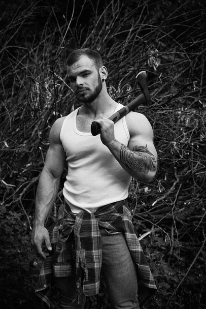Black and white photo of handsome young man holding hatchet posing outdoors - Photo, Image