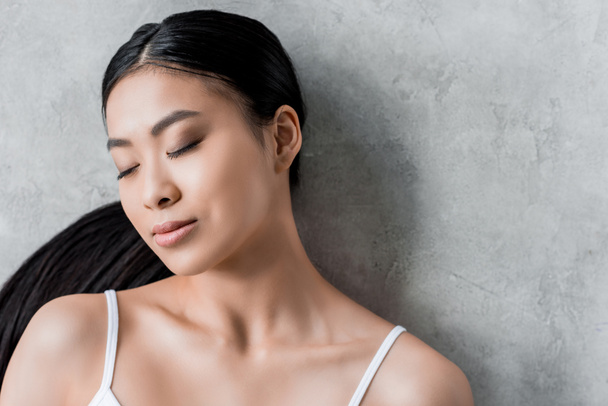 pretty brunette asian girl with closed eyes, on grey - 写真・画像