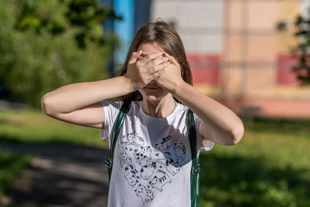 A little teenage girl covered her eyes with her hands. In the summer in the open air. A bright sunny day. The concept of reluctance to see. Very bright sun. The game of hide and seek After school. - Фото, зображення