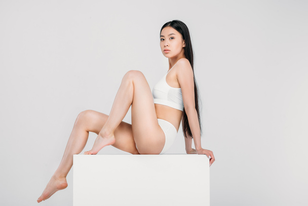 elegant asian girl posing in lingerie on white cube, isolated on grey  - Фото, изображение