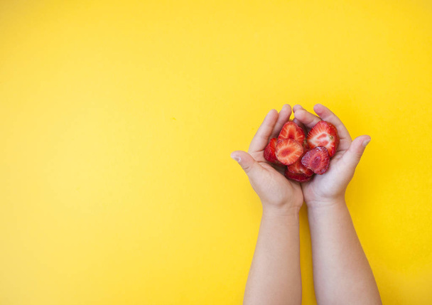 Manos de niño sosteniendo un cuenco rosado lleno de hermosas fresas jugosas frescas sobre fondo amarillo brillante con espacio de texto
. - Foto, Imagen