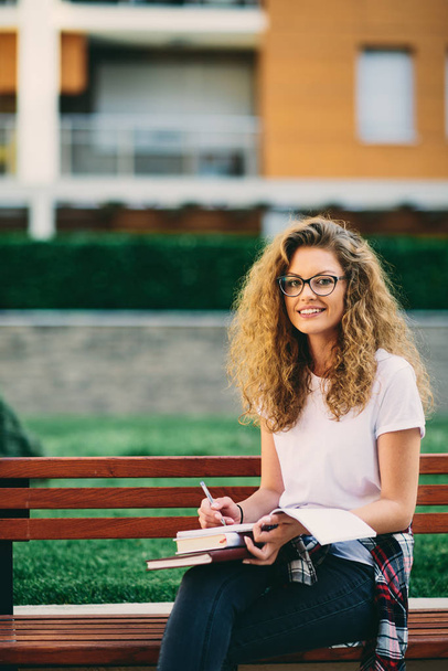 Жінка-студент бризкає есе, сидячи на лавці в кампусі
. - Фото, зображення