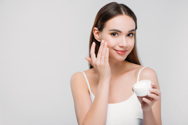 beautiful girl applying cosmetic cream on face, isolated on grey - Foto, Imagem
