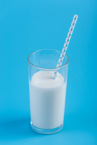 A glass of fresh milk with a straw on a blue background. Colorful minimalism. The concept of healthy dairy products with calcium - Photo, Image