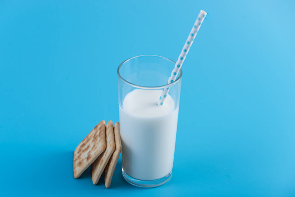 Стакан свежего молока с соломинкой и печеньем на синем фоне. Красочный минимализм. Концепция здоровых молочных продуктов с кальцием
 - Фото, изображение