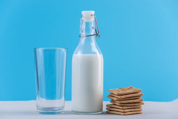 Botella de vidrio de leche fresca y galletas sobre fondo azul. Minimalismo colorido. El concepto de productos lácteos saludables con calcio
 - Foto, Imagen
