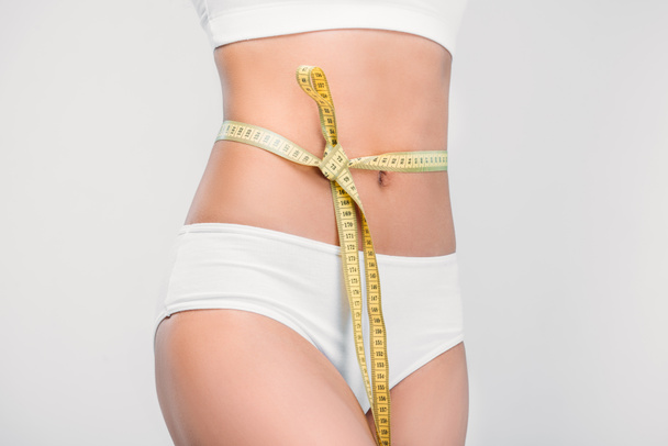 partial view of slim girl in white underwear with measuring tape on waistline, isolated on grey - Foto, immagini