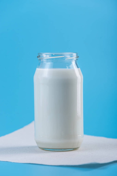 Mavi zemin üzerine taze süt ile cam şişe. Renkli minimalizm. Kalsiyum sağlıklı süt ürünleri kavramı - Fotoğraf, Görsel