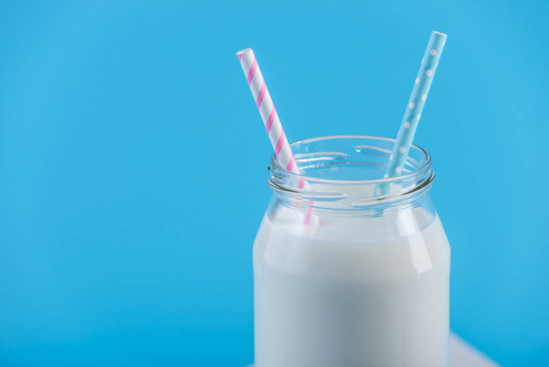 Glass bottle of fresh milk with two straws on blue background. Colorful minimalism. The concept of healthy dairy products with calcium - Photo, Image