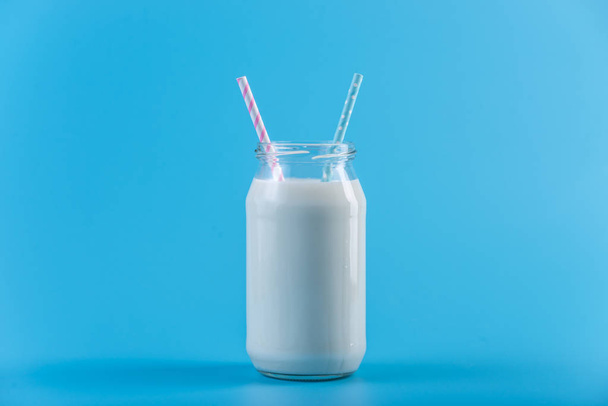 Glasflasche mit frischer Milch mit zwei Strohhalmen auf blauem Hintergrund. bunter Minimalismus. das Konzept gesunder Milchprodukte mit Kalzium - Foto, Bild