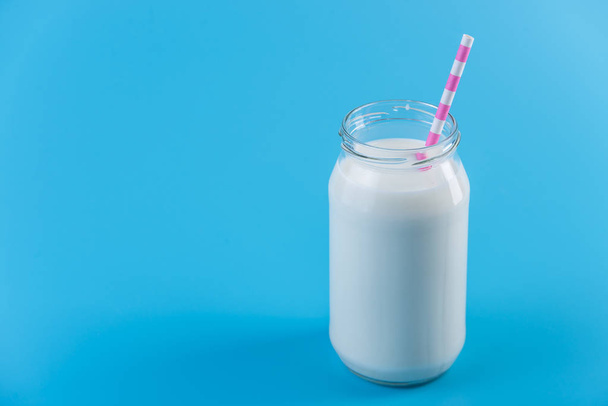 Стеклянная бутылка свежего молока с соломой на синем фоне. Красочный минимализм. Концепция здоровых молочных продуктов с кальцием
 - Фото, изображение