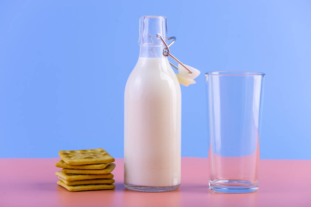 Glazen fles van verse melk en koekjes op pastel achtergrond. Kleurrijke minimalisme. Het concept van gezonde zuivelproducten met calcium - Foto, afbeelding