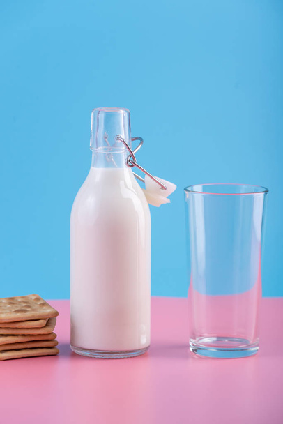 Botella de vidrio de leche fresca y galletas sobre fondo pastel. Minimalismo colorido. El concepto de productos lácteos saludables con calcio
 - Foto, Imagen