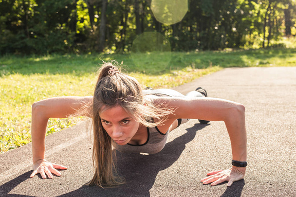 Nuori fit nainen käyttää tekemällä push-ups ulkona
 - Valokuva, kuva