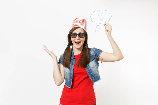 Portrait of Smiling woman in 3d glasses with bucket for popcorn on head watching movie film holding say cloud with lightbulb, idea and spreading hands isolated on white background. Emotions in cinema - Photo, Image