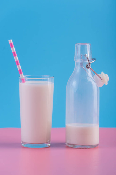 Γυάλινο μπουκάλι φρέσκο γάλα και ένα ποτήρι με ένα Καλαμάκι σε παστέλ φόντο. Πολύχρωμο μινιμαλισμό. Η έννοια του υγιούς γαλακτοκομικά προϊόντα με ασβέστιο - Φωτογραφία, εικόνα