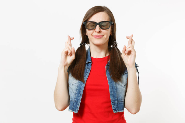 Portrait of young smiling pretty woman in 3d glasses and casual clothes watching movie film, keeping fingers crossed and eyes closed isolated in studio on white background. Emotions in cinema concept - Photo, Image