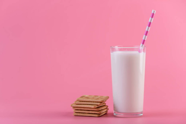 Bir bardak taze süt bir saman ve çerezler üzerinde pembe bir arka plan ile. Renkli minimalizm. Kalsiyum sağlıklı süt ürünleri kavramı - Fotoğraf, Görsel