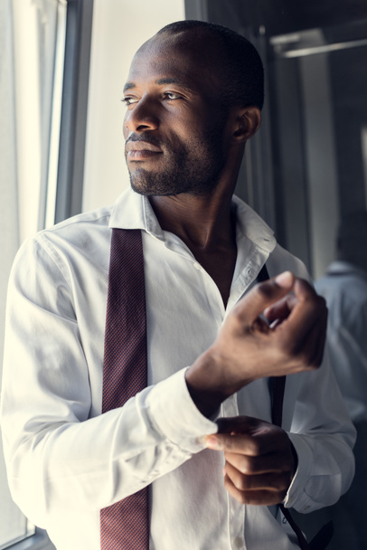 close-up portrait of thoughtful young businessman in white shirt buttoning cufflinks and looking away - Zdjęcie, obraz