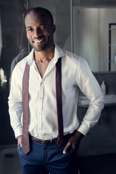 usměvavý mladý podnikatel v bílé košili s kravatou, visí na ramenou v koupelně - Fotografie, Obrázek