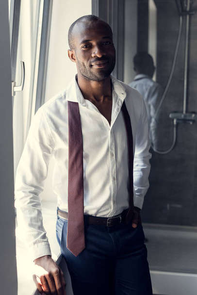 handsome young businessman in white shirt with tie hanging on shoulders at bathroom - Fotó, kép