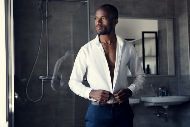 thoughtful businessman buttoning his white shirt at bathroom and looking away - Photo, Image