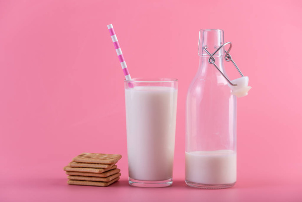 Γυάλινο μπουκάλι φρέσκο γάλα και μπισκότα σε ροζ φόντο. Πολύχρωμο μινιμαλισμό. Η έννοια του υγιούς γαλακτοκομικά προϊόντα με ασβέστιο - Φωτογραφία, εικόνα