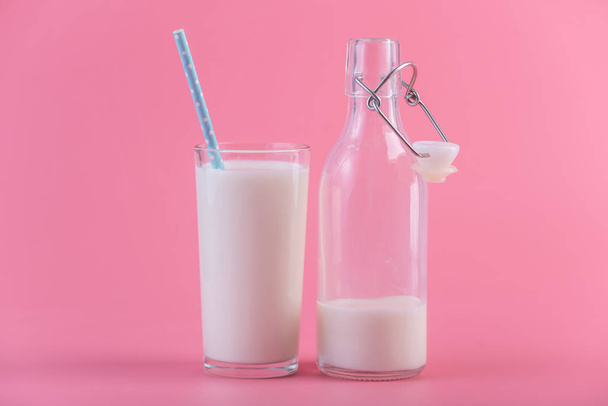 Bottiglia di vetro di latte fresco e un bicchiere con una cannuccia su sfondo rosa. Minimalismo colorato. Il concetto di latticini sani con calcio
 - Foto, immagini